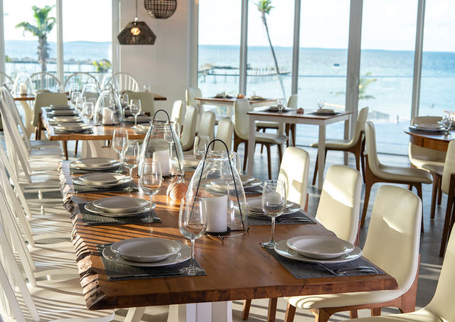 A long table with place settings in front of floor to ceiling windows with an ocean view.
