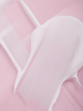 White creamy lotion product smeared on a soft pink background.