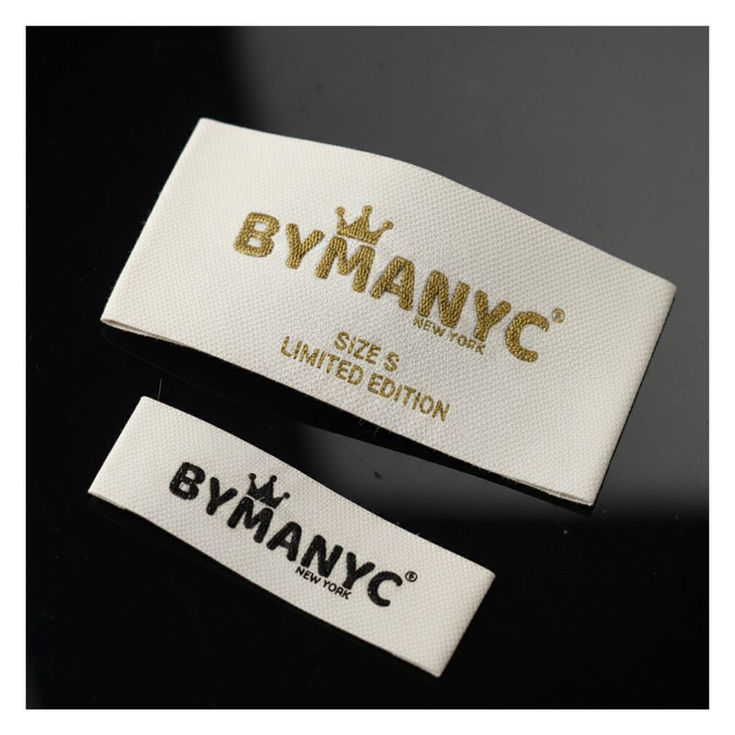 Two white fabric labels: BYMANYC, SIZE S, LIMITED EDITION, gold lettering.
