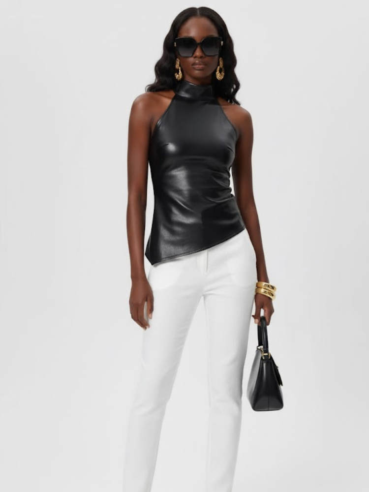 Woman modeling black faux leather halter top, white pants, handbag.