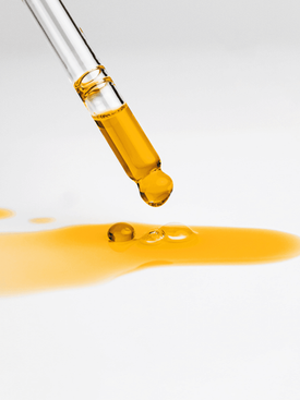 Glass dropper dispensing golden yellow serum onto a white surface.