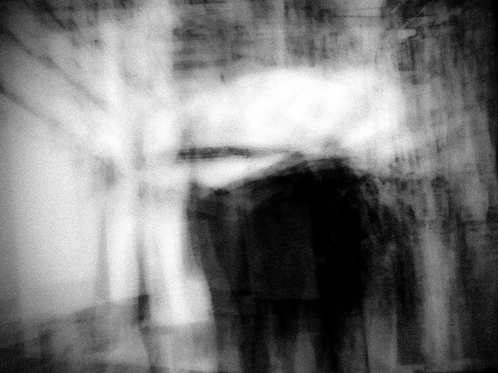 Blurry black-and-white abstract scene with a bright light and dark doorway-like shape, creating a ghostly mood.