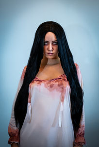 A woman with long black hair stares forward with a bloodied night gown.