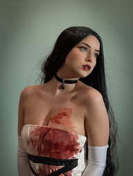 A woman poses in a formal white dress stained with blood.