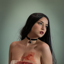 A woman poses in a formal white dress stained with blood.
