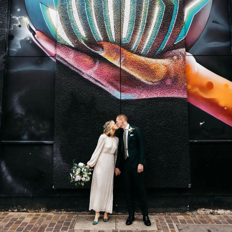 a bride and groom kiss in front of a large mural