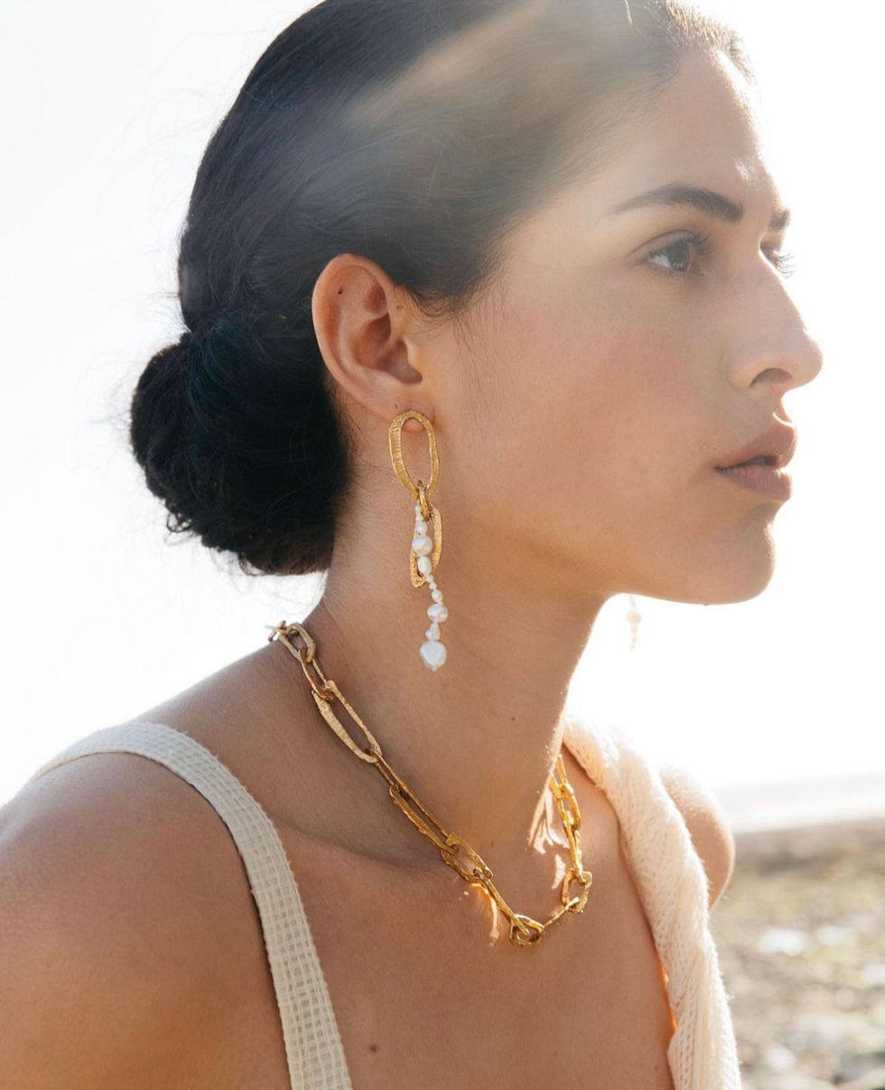 a woman wearing a gold chain necklace and earrings