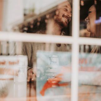 A couple embraces amidst the dimly lit ambiance of Cool Beans Bar & Grill, their smiles radiant in the cozy atmosphere. In another photo, they share a tender moment, bathed in the warm glow of the bar's neon lights. Each image captures the raw authenticity and deep connection between the couple as they celebrate their love in this unique setting.