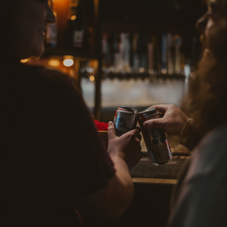 A couple embraces amidst the dimly lit ambiance of Cool Beans Bar & Grill, their smiles radiant in the cozy atmosphere. In another photo, they share a tender moment, bathed in the warm glow of the bar's neon lights. Each image captures the raw authenticity and deep connection between the couple as they celebrate their love in this unique setting.