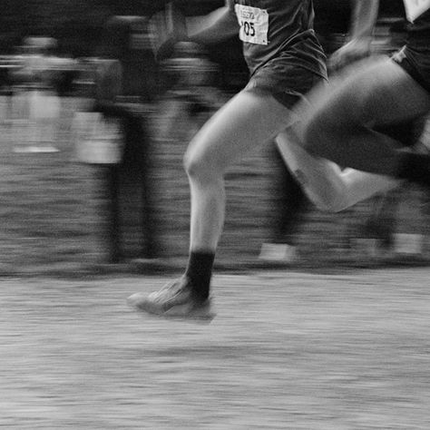 Runners in motion, captured in blurred black and white. Legs are mid-stride. A crowd watches in the park. Athlete numbers barely visible.