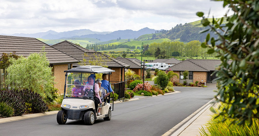 Residents riding a golf cart down a quiet street at Longridge retirement village