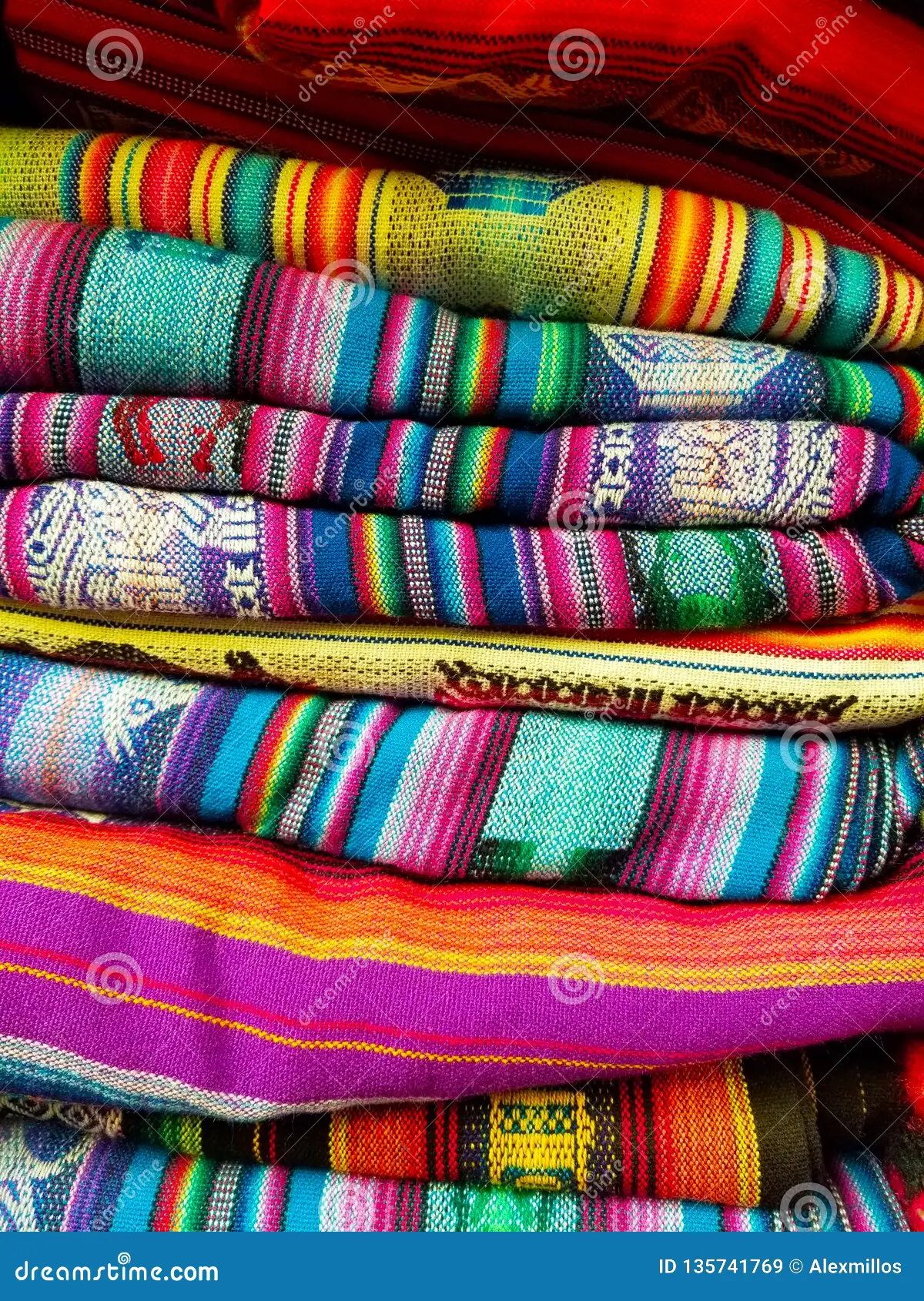 Beautiful array of bright colourful knitted blankets stacked on top of each other. The colours include, bright pinks, purples, blues, greens, yellows, oranges, reds, all weaven together to display these beautiful throw blankets.