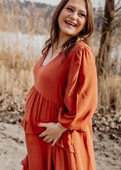 Schwangere Frau im orangenem Kleid steht am Heidesee, umgeben von Schilf und Wasser, ein wunderschöner Moment der Babybauchfo
