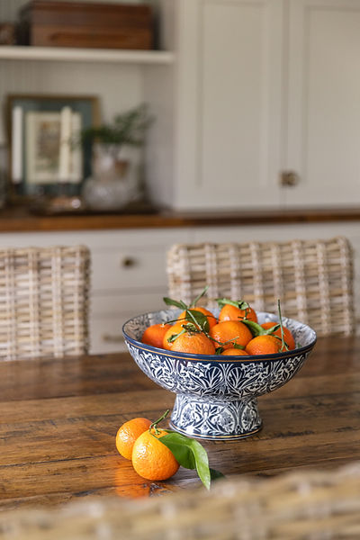 blue and white bowl with seasonal oranges on top of a dining table.