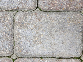Close-up of textured, gray stone pavement with moss and grass growing between the cracks, displaying a natural, rustic pattern.