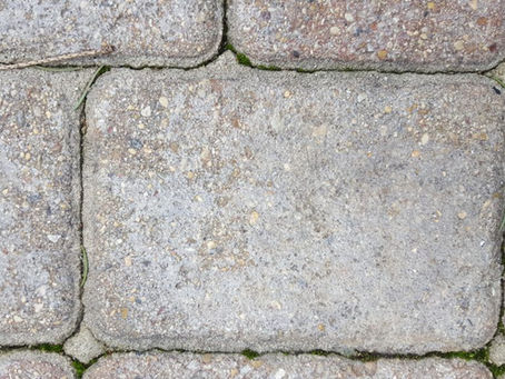 Close-up of textured, gray stone pavement with moss and grass growing between the cracks, displaying a natural, rustic pattern.