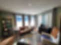 Picture of office, green room with bright lighting. there are books, chairs and brown leather couch.