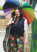 Margit van der Zwan plays the cello at the Manchester flower festival holding a rainbow coloured umbrella