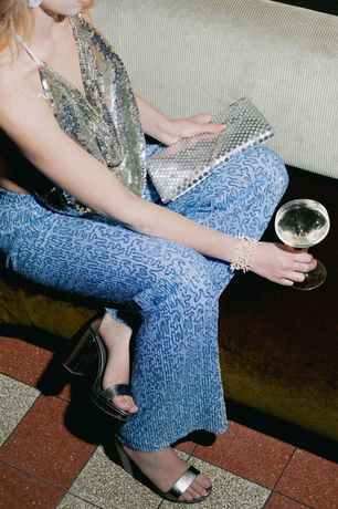 Woman in light blue glitter trousers and a silver metallic top with clutch, party outfit rented from RENTGLAM in Amsterdam