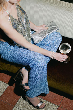 Woman in light blue glitter trousers and a silver metallic top with clutch, party outfit rented from RENTGLAM in Amsterdam
