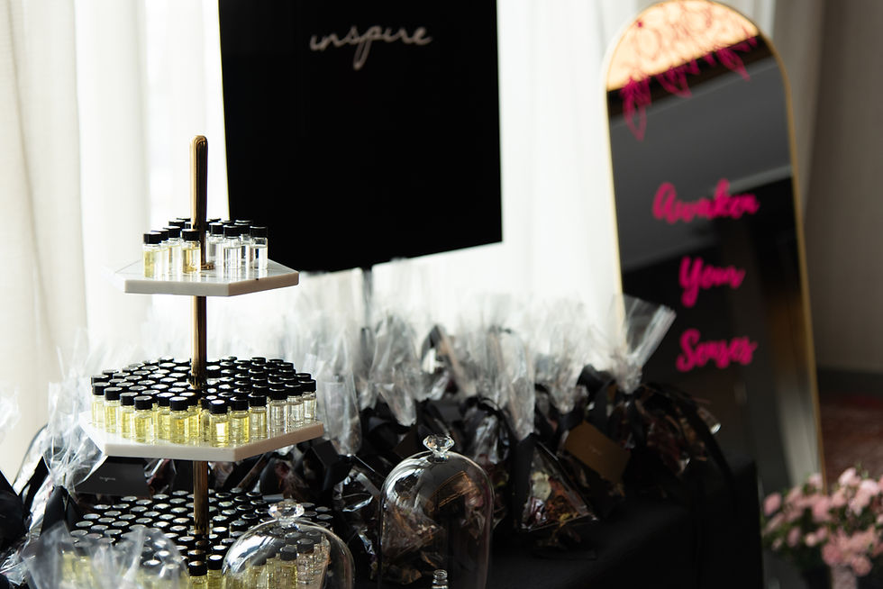 Tiers of small bottles with scents inside with gift bags on the table next to it.