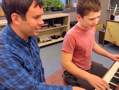Piano teacher sitting next to student at the piano practicing