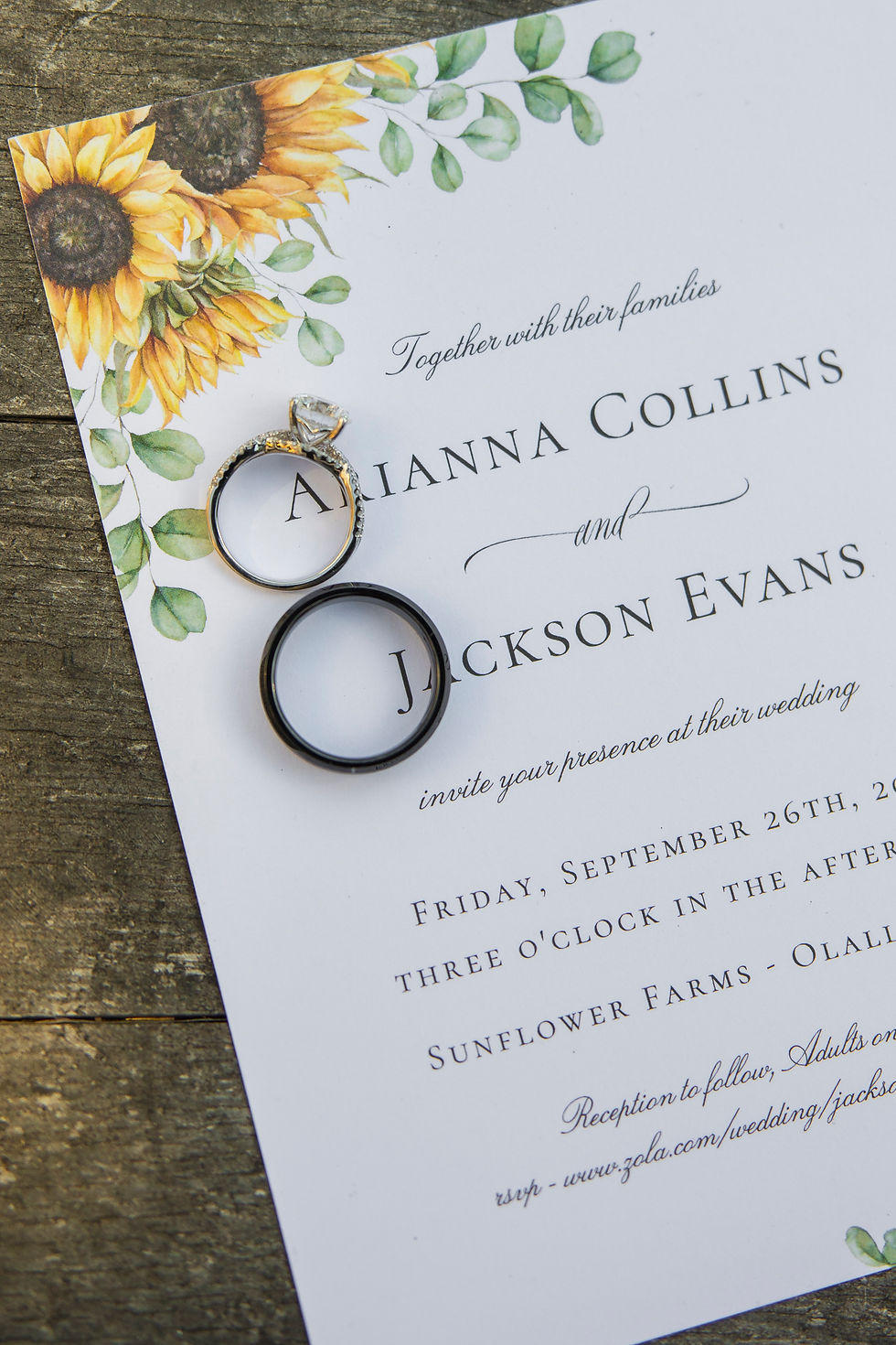 Wedding invitation on wood with sunflower design, two rings placed on it, inviting to Arianna and Jackson's wedding at Sunflower Farms. flatlay