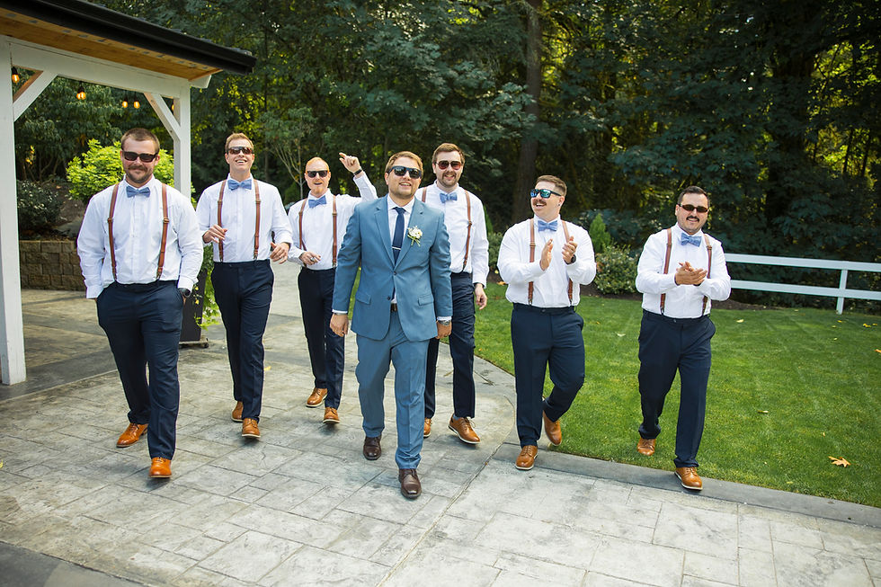 Groom in a blue suit and groomsmen in white shirts with bow ties walk joyfully outside, wearing sunglasses, by Sage and Soul Photography