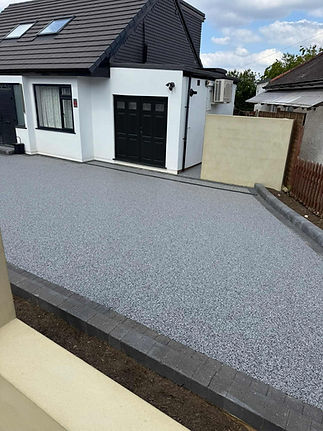 A freshly installed, speckled grey resin driveway curves towards a white house with black garage doors
