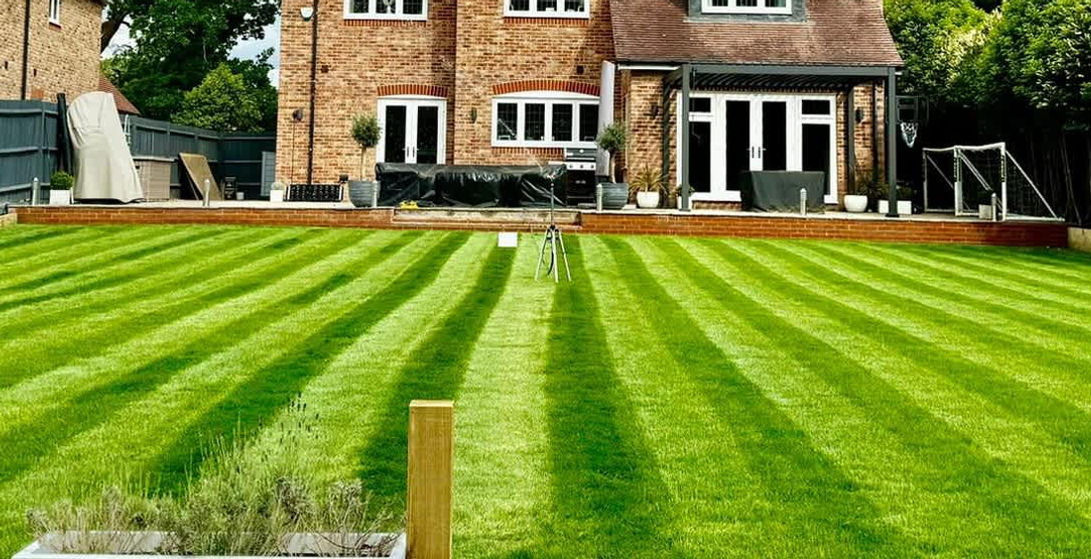 A manicured lawn with stripes leading to a large brick house with a wooden deck