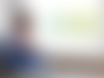 A blurred image of a young child sitting on the floor by a window with knees drawn to their chest, conveying feelings of sadness, isolation, and emotional vulnerability in a quiet indoor setting.