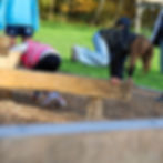 Kinderen spelen buiten op een houten klimtoestel in een park, omringd door groen gras en herfstbomen. Casual en vrolijke sfeer.