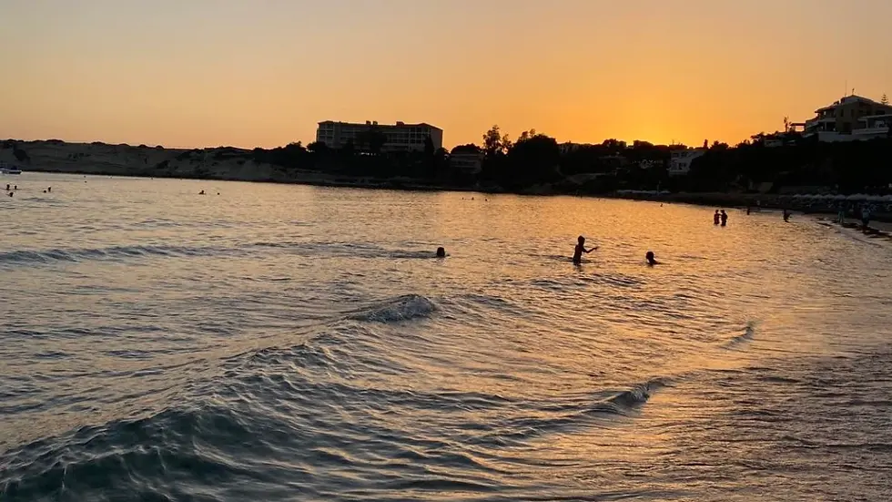Sunset across a calm Cyprus bay with swimmers and soft waves near the shoreline