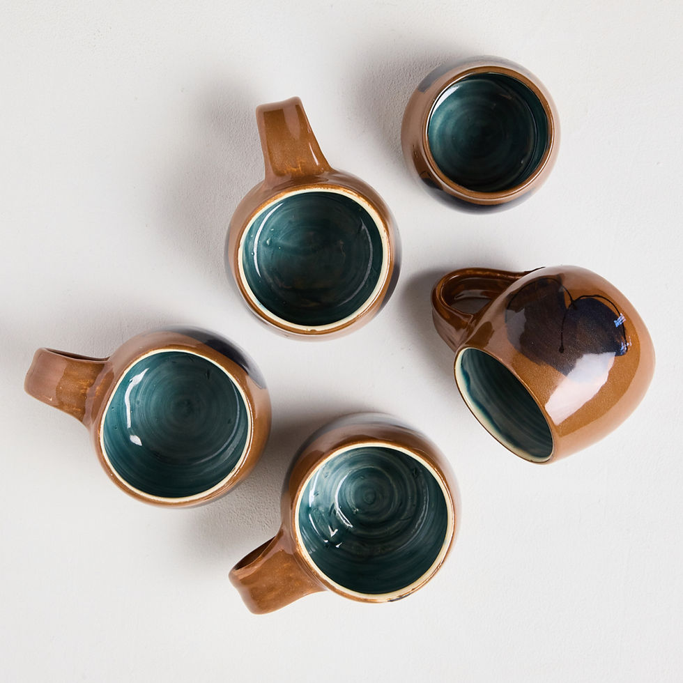 Handmade stoneware mugs with glossy brown exterior and deep green glazed interior, photographed from above in a Cornwall pottery studio