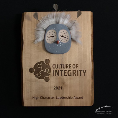 This is an image of a Birch award plaque finished in natural tones. The plaque has live edges showing from the front, and is laser engraved with the logos and descriptions. A Yup'ik stylized Yup’ik Owl maskette is affixed above the engraving, finished in blue grey tones with reindeer fur and feather attachments.