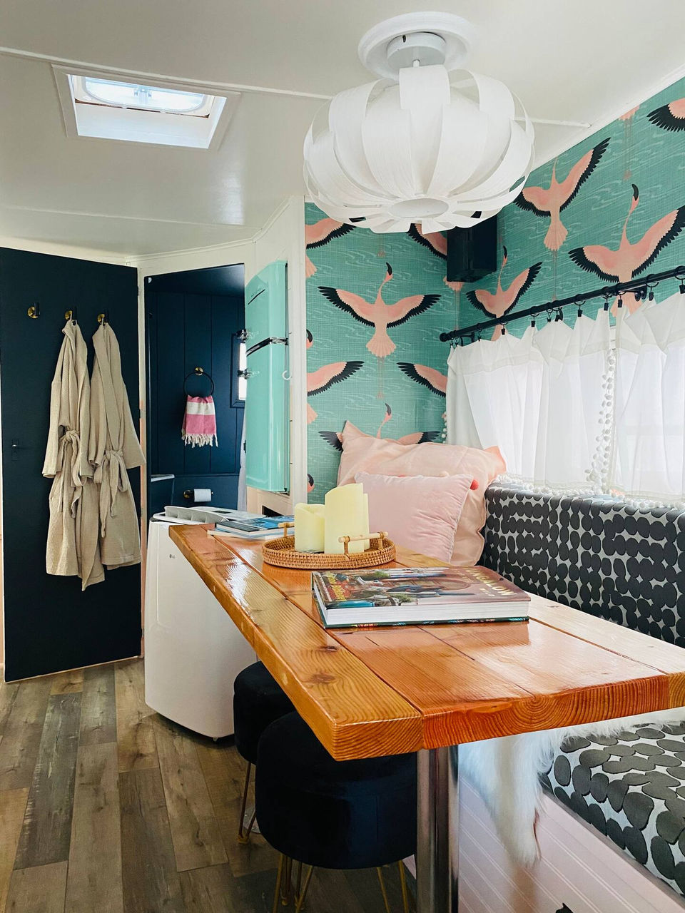 View of the table and bench/sitting area inside Poppy, the Vintage Glamper. The beautiful, vibrant wall paper and vintage refrigerator give off the boho vibe.