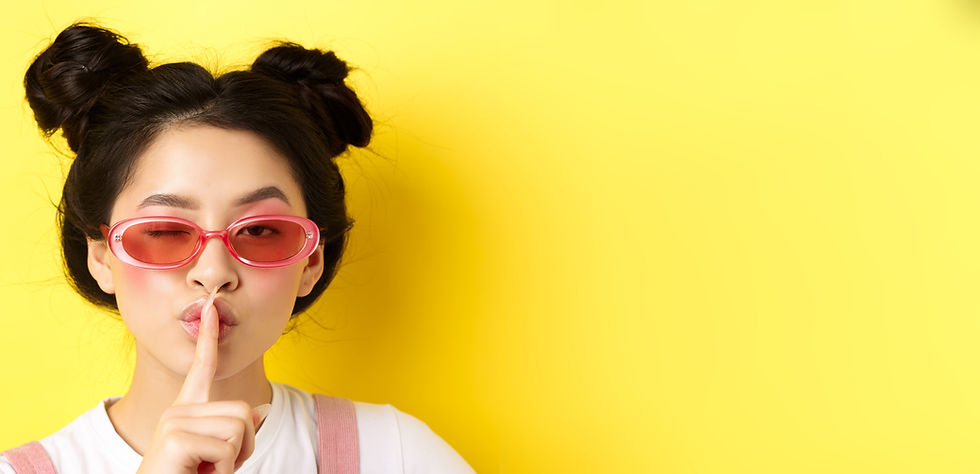 Young adult with hair puffs, pinkish sun glasses, and "shhhhing"