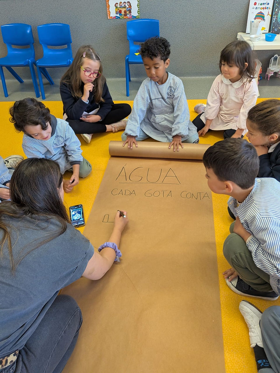 Crianças em roda com a mãe Maria João junto ao painel no projeto sobre a água e sustentabilidade