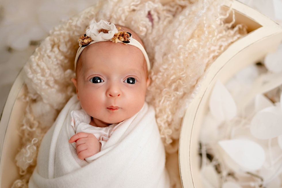 Neugeborenes in cremefarbener Decke gewickelt, trägt Stirnband mit Blume. Weiches, neutrales Hintergrunddesign. Friedliche Stimmung.