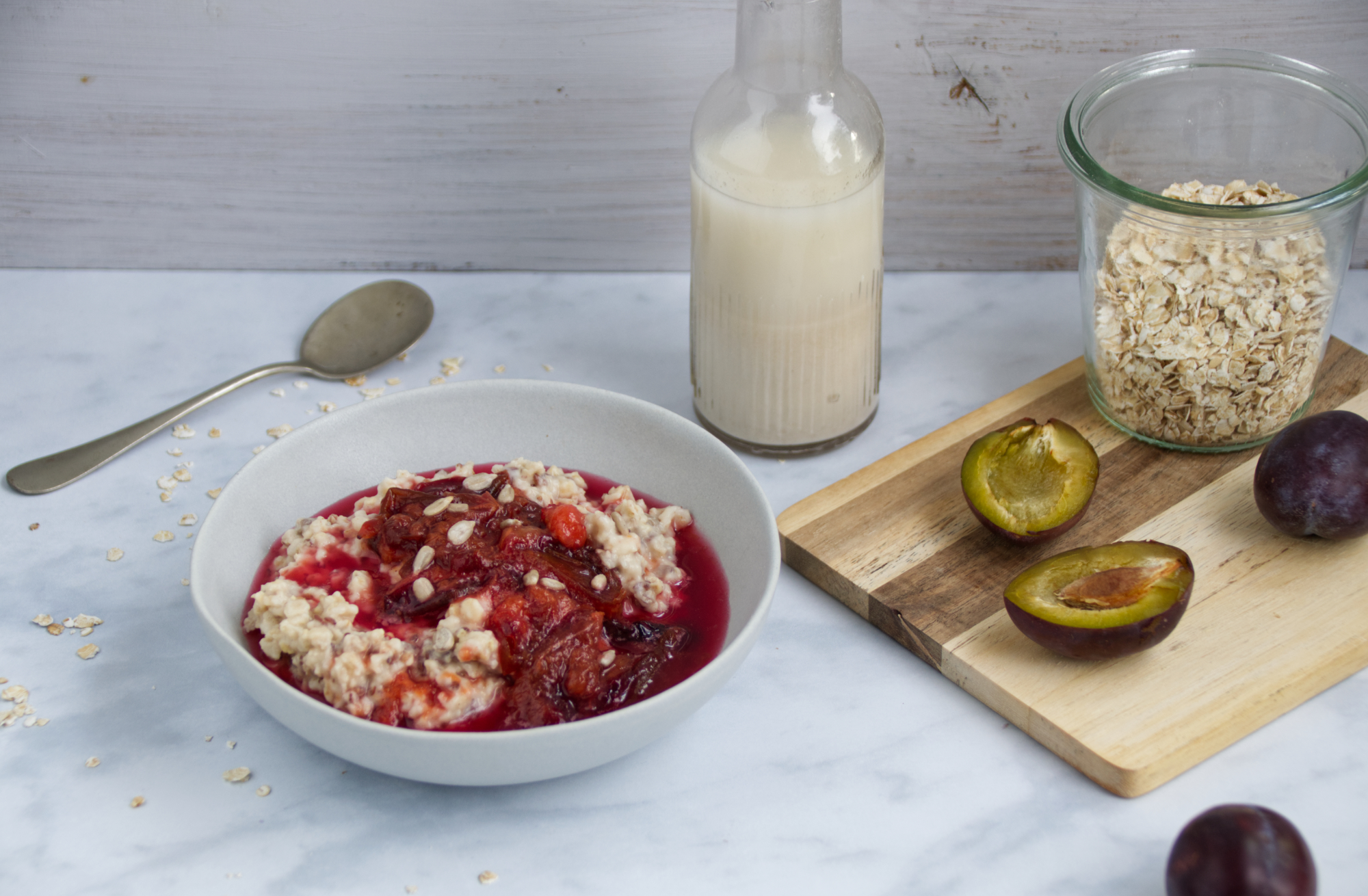Poriddge in einer mit Pflaumenkompott dazu eine Flasche Haferdrink und Pflaumen