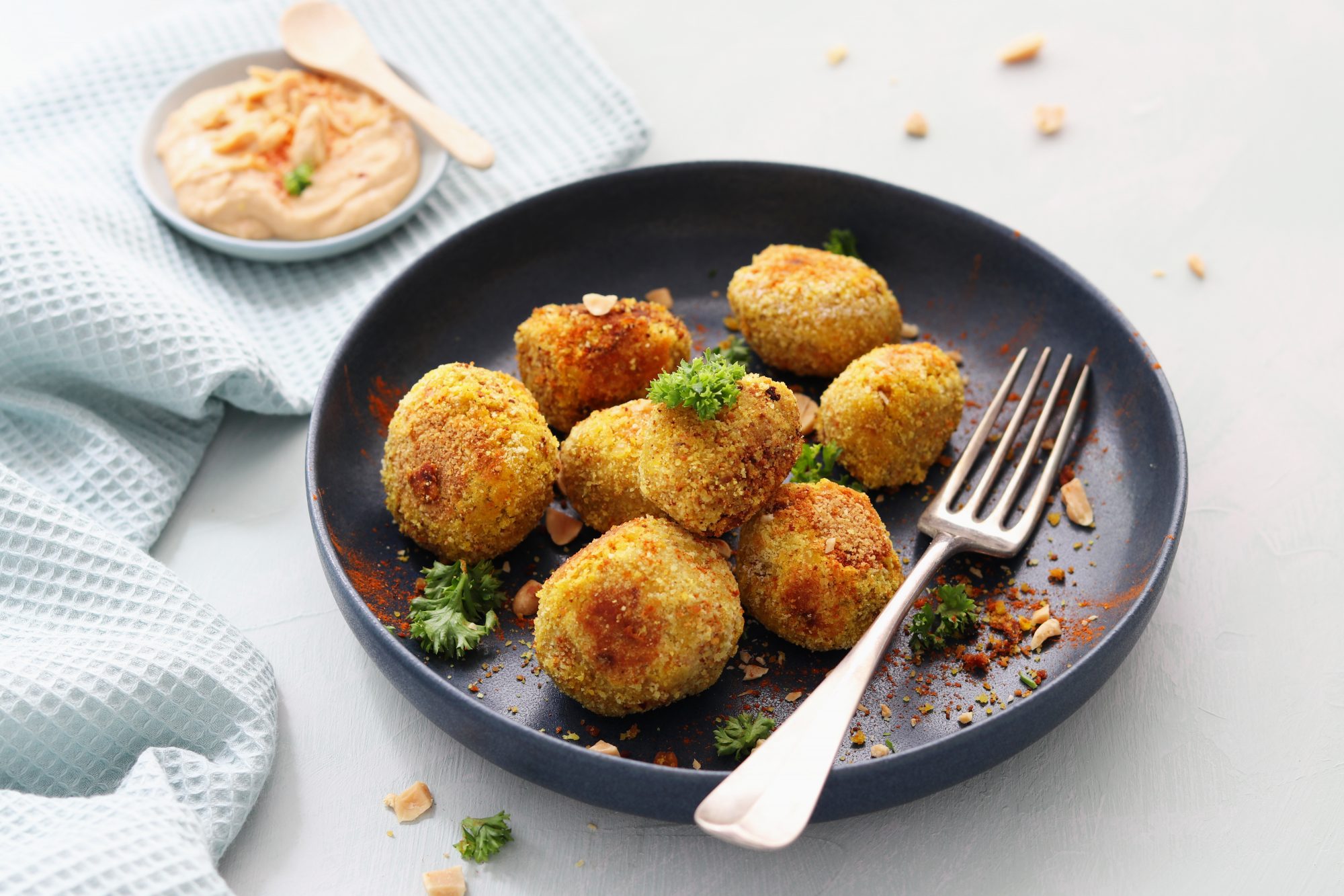 kleine hellbraune Linsenbällchen ligeen mit einer Gabel auf einem Teller, daneben steht ein Schälchen mit einem hellen Dip