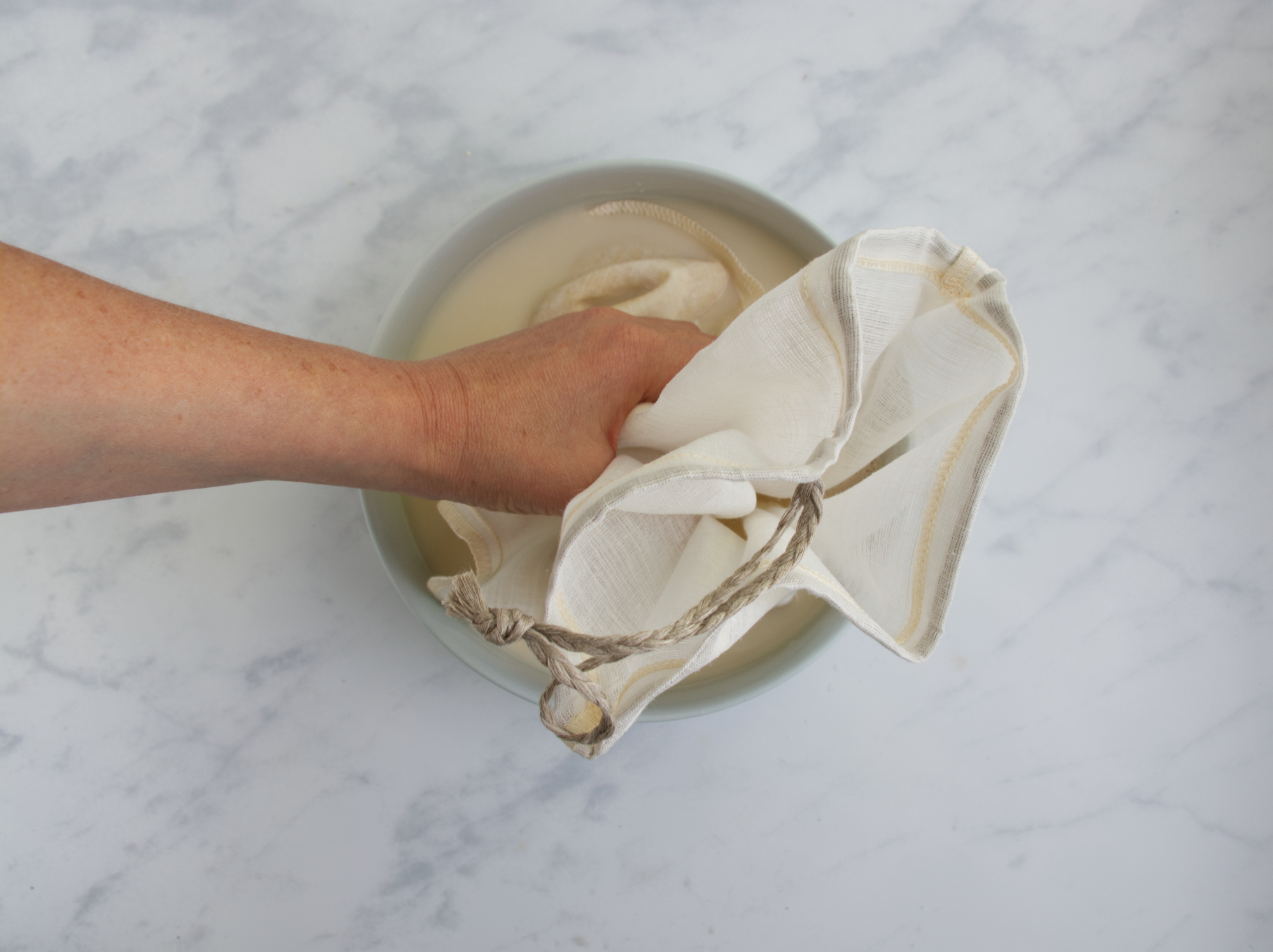 Eine Hand quetsch einen Leinen beuetel mit eingeweichten Haferflocken