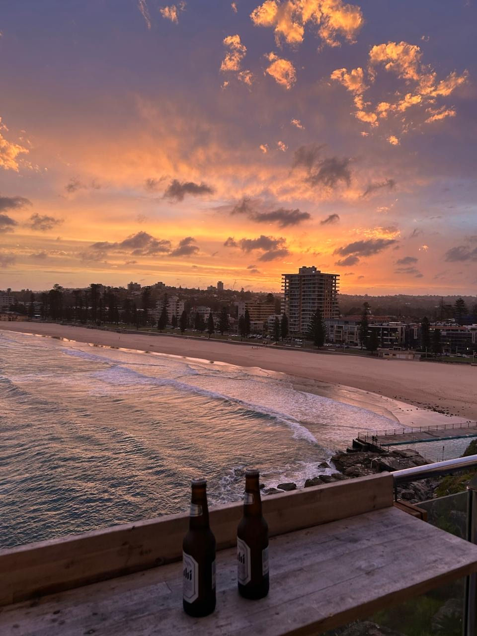 Vista de Manly Beach en Sydney con el mar, edificios y dos cervezas frente a la playa