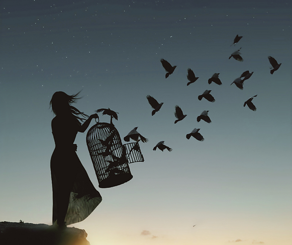 Silhouette of a woman at sunrise releasing birds from a birdcage