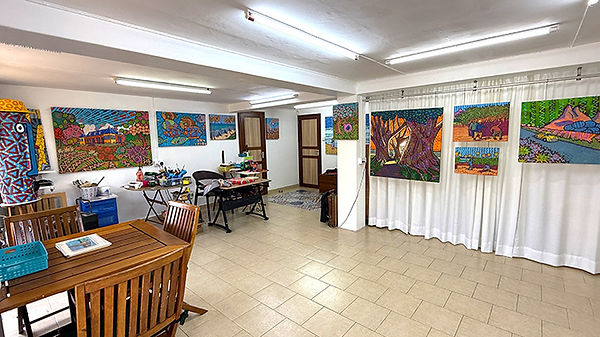 Interior of Pascal Lagesse's art studio in Curepipe, Mauritius, with colourful Zafer style paintings hanging on the walls and a work table in the foreground.