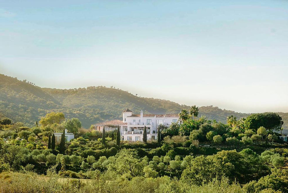 White villa nestled among lush greenery and trees, set against a backdrop of rolling hills under a clear blue sky, conveys serenity and luxury at Viluz Wellbeing Adults Only Resort in Marbella, Spain