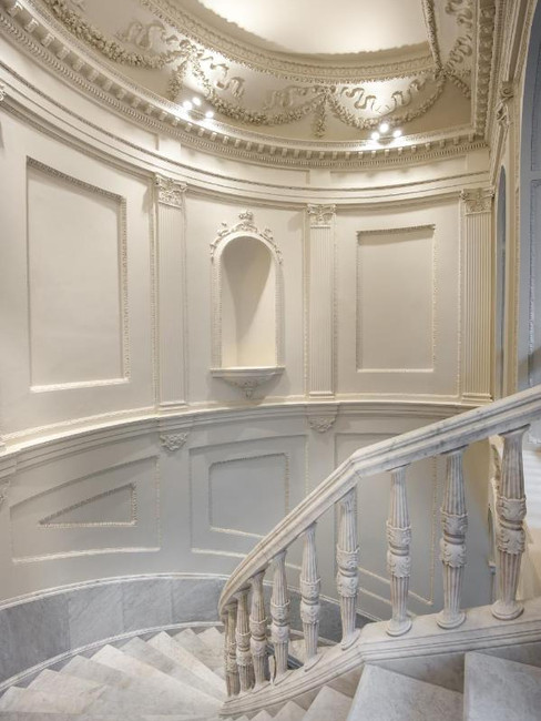 Elegant spiral staircase in a spacious, ornate white hallway with intricate wall moldings and soft lighting at luxury hotel Mercer Sevilla
