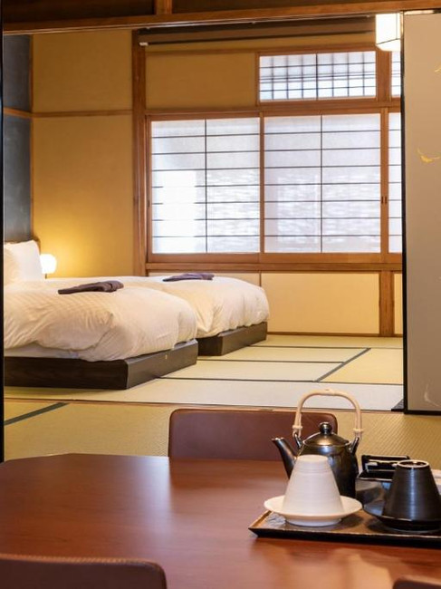A traditional Japanese room at Gion Kyoka ryokan featuring a bed and two chairs, showcasing minimalist design and elegance.