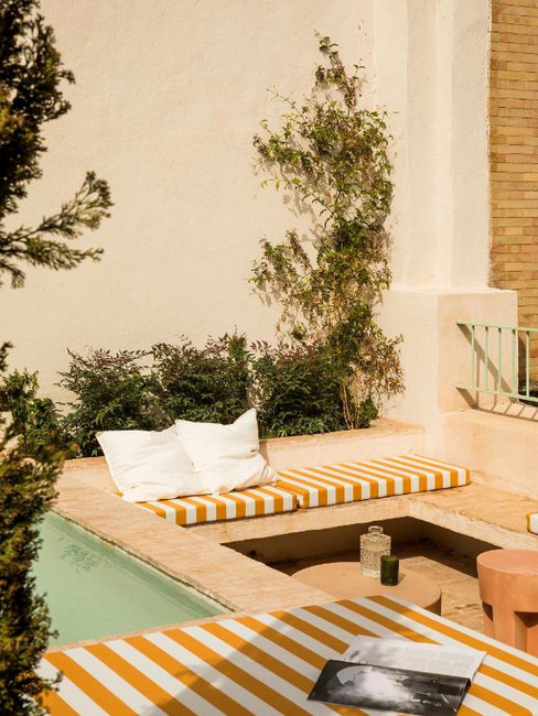 Stylish outdoor lounge with striped cushions by a small pool, surrounded by greenery and a coffee table with magazines at Boscos Apartments, a hotel with private pools in Seville