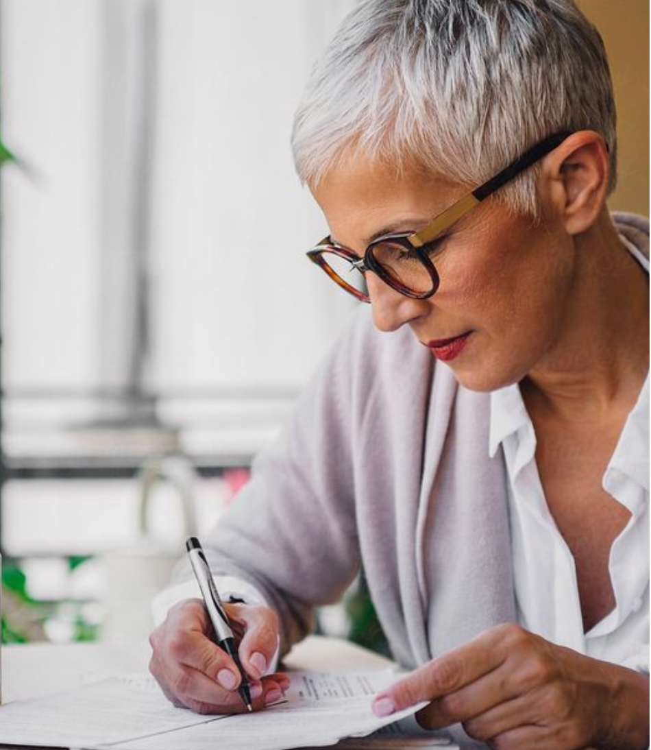 white woman with short hair and glasses writing in journal